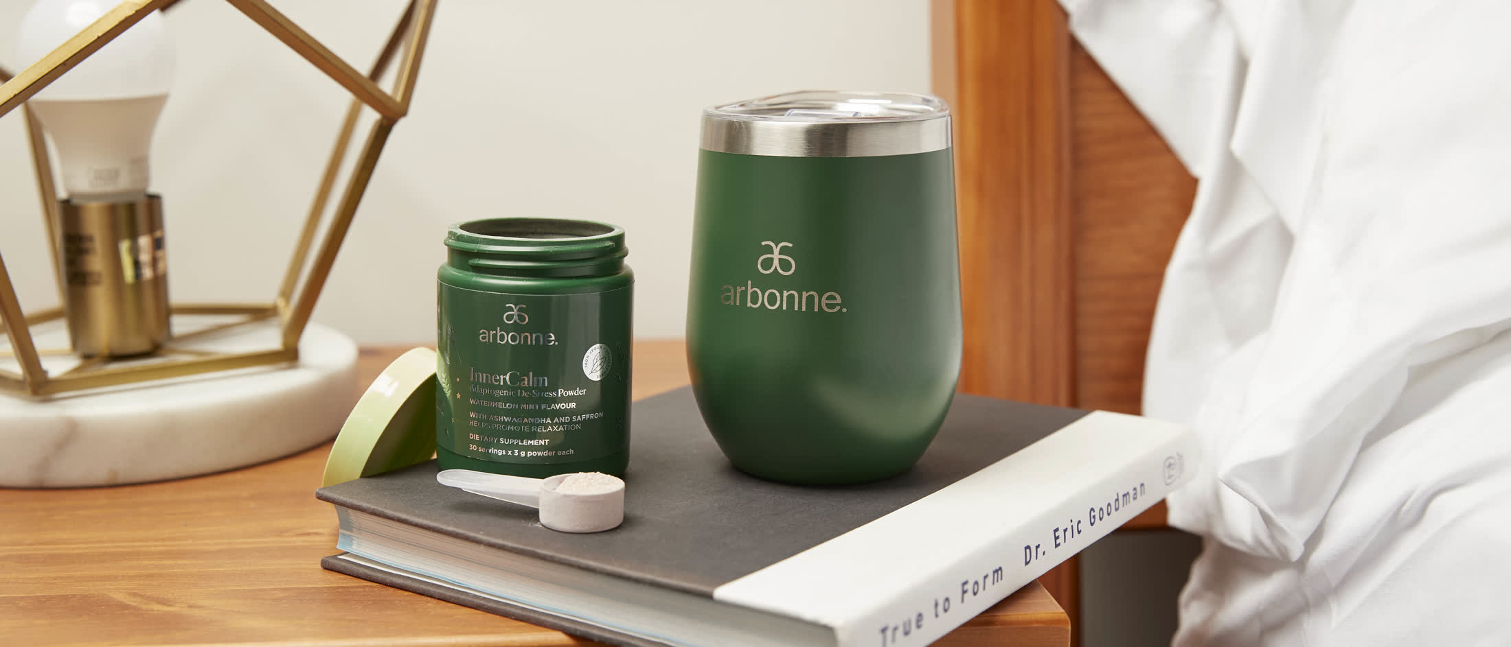 Arbonne InnerCalm jar and tumbler on a bedside table with a book